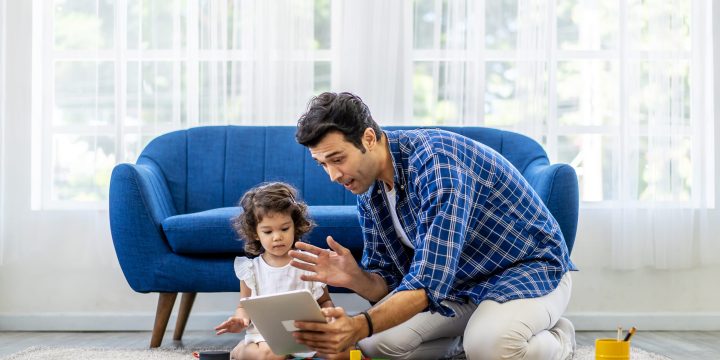 Portrait of positive father making virtual video call with mother using tablet, while the little daughter was playing with colorful wooden blocks