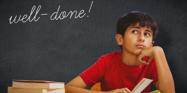 The word well-done! and thoughtful boy reading book in library against blackboard